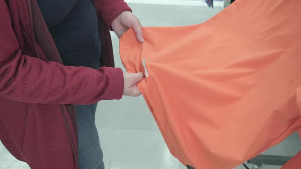 Pregnant Woman Chooses Orange Jacket with Reflective Stripe in Store to Buy