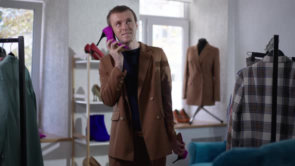 Funny Cheerful Caucasian LGBT Man Having Fun Using Purple Highheels As Phone Talking Smiling alt
