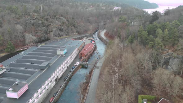 Curved Canal Next to Industrial Building and Forest Forward Aerial