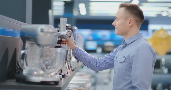 A Man Chooses a Blender in the Appliances Store Kitchen Appliances in His Hands and Considers the alt