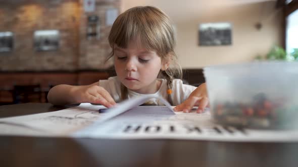 Little Beautiful Girl Coloring a Picture in a Cafe