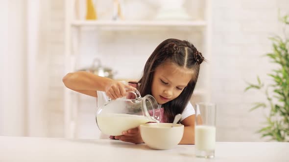 Child Pours Milk Into a Bowl of Cereal in the Kitchen