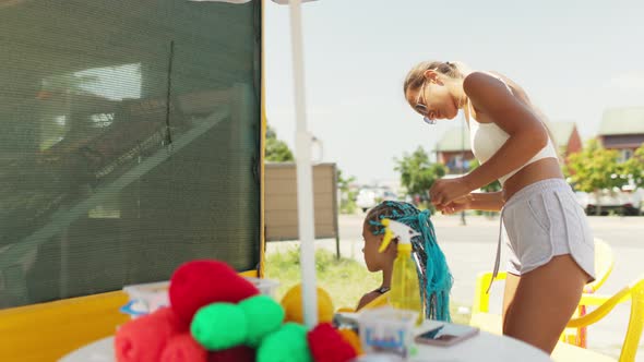 Many Threads and Ribbons Lie on the Table Against the Background of a Girl Whose African Braids are alt