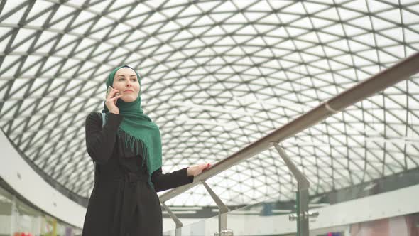 Pretty Muslim Woman in a Hijab with a Backpack Goes To the Shopping Center and Talks on the Phone alt