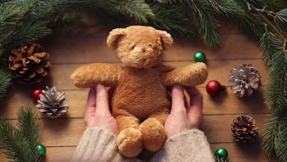 Female hands holding Christmas teddy bear toy on wooden table.