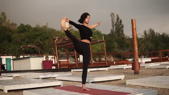 Woman Practicing Yoga on Mat on the Beach Performing Yoga Asanas or Stretching Legs Leaning Torso alt