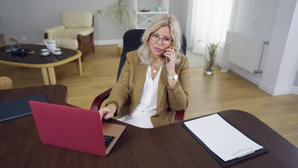 Smiling Slim Beautiful Caucasian Woman Sitting at Table with Laptop Talking on Phone alt
