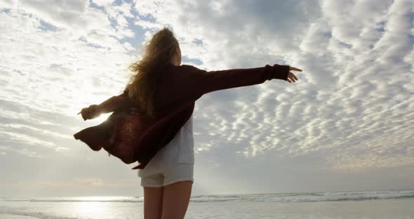 Rear view of young woman with arms outstretched looking at sea on the beach 4k alt