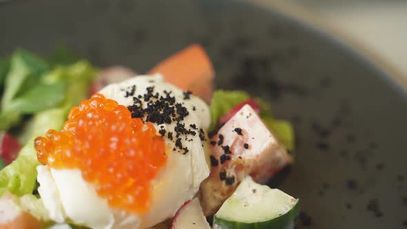 Closeup of a Salad with Poached Egg and Red Caviar on a Black Plate