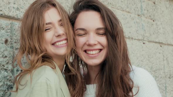 Two young beautiful smiling hipster girls in trendy clothes posing outdoors alt