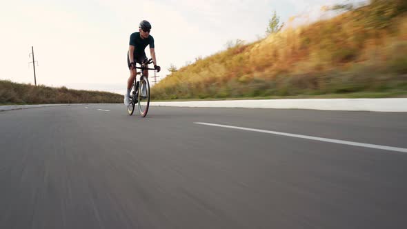 Young fit man cycling on road downhill alt