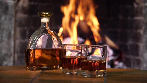 Bottle and Glasses with Whiskey or Cognac on the Background of Fire in the Fireplace alt