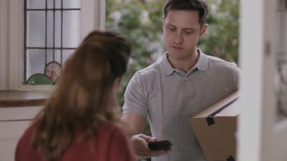 Delivery man delivering parcel at home, woman signing for parcel at front door