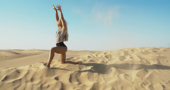Woman is Throwing Sand on the Wind in the Desert While Kneeling on a Dune alt