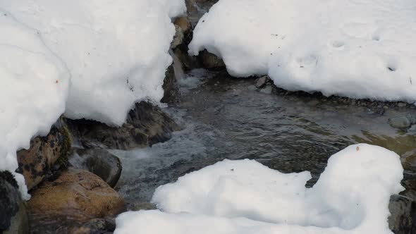 CLOSE UP Glaciar water brook flowing hardly through snow covered rocks alt