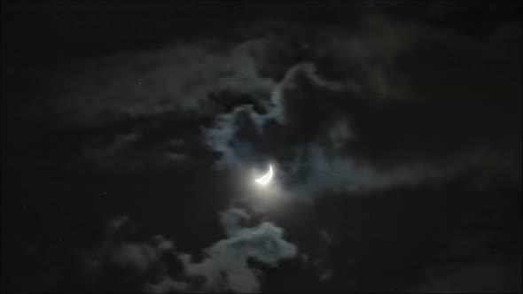 Time lapse: the moon lighting through clouds in dark night sky alt