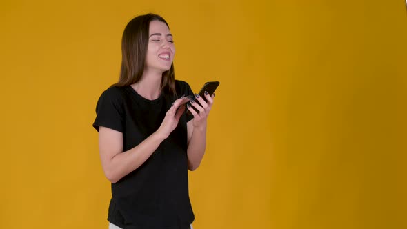 Young Happy girl using smart phone and texting online chat with smile isolated on yellow background.