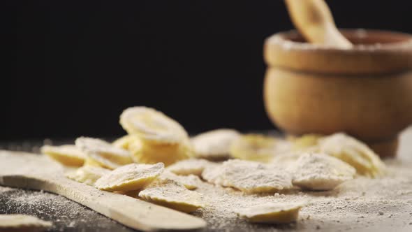 Tasty raw ravioli with flour and basil on wood table rotating alt