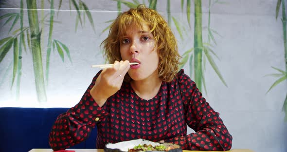 European Bigeyed Young Woman in a Chinese Cafe is Eating Looking at the Camera and Enjoying an Asian alt