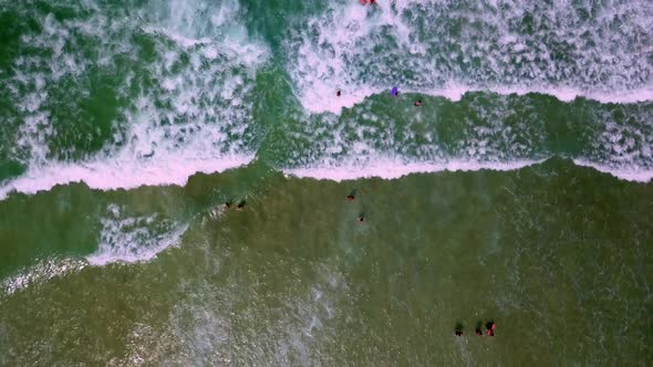 Aerial top down shot of people walking through the sea waves breaking on the beach alt