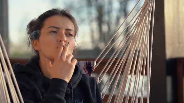 Portrait of a Beautiful Young Woman Smoking a Cigarette in the Evening on the Veranda