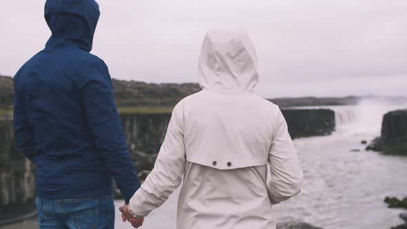 Back View of Young Hipster Couple Stranding Near the Powerfull Waterfall in Iceland and Enjoying the alt