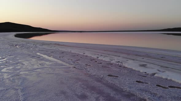 Aerial View of Flying Over the Salty Shore of Pink Salt Lake in the Evening at Dusk Blue Sky alt