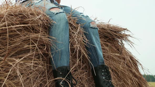 Teenager Boy in Jeans and Checkered Shirt Sitting on Haystack on Countryside Field alt