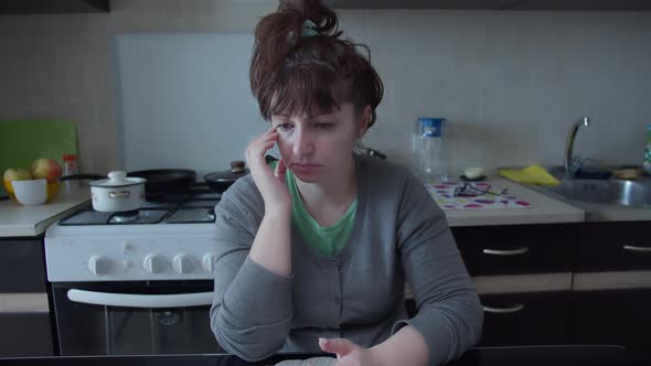 Brunette Woman with Headache Sitting in the Kitchen at Home Tired Sad Woman