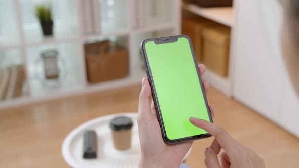 Woman holding mockup smartphone green screen with type message on the sofa at home
