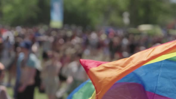 The LGBTQ rainbow flag waving in slow motion with people in a pride parade in the background