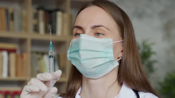 Female Doctor with a Medical Mask and Protective Gloves Holding Syringe with Medicine alt