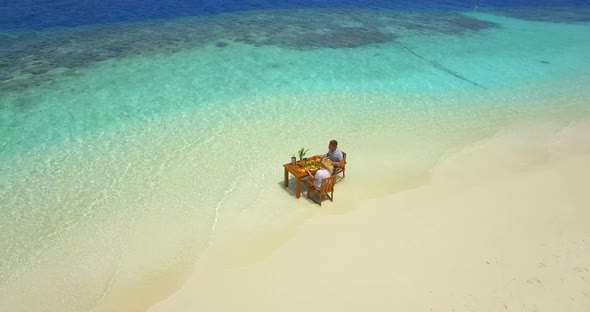 Aerial drone view of a man and woman eating breakfast on a tropical island beach. alt