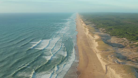 Beautiful Empty Beach at Golden Hour Going Endless Into the Distance with Green Woods and Blue Ocean alt