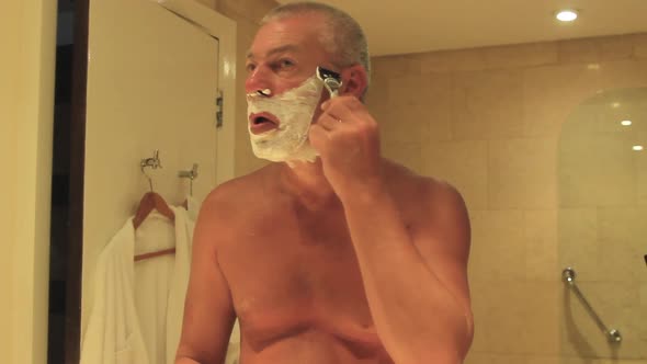 A Man Shaves His Beard with a Razor While Standing in Front of a Mirror