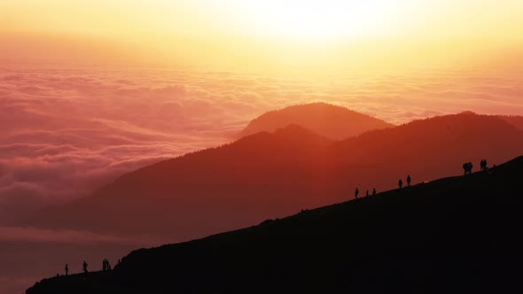 Silhouettes Walk on Mountain Crest Against Hills at Sunset