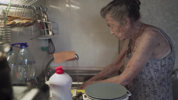 Lonely Sad Senior Woman 90 Years Old with Gray Hair Forced to Wash Dishes with Her Hands Due to alt
