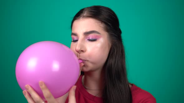 Young Woman Inflates a Balloon Isolated on Blue Background