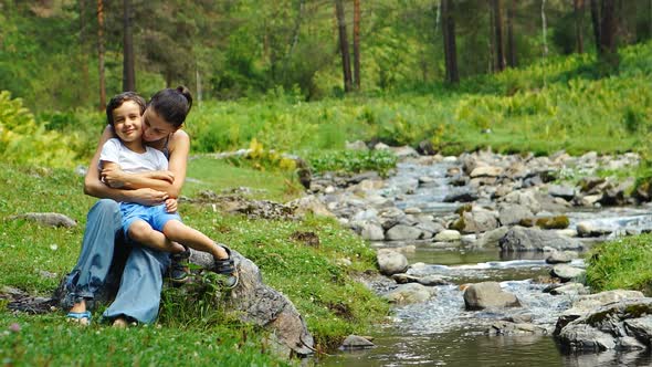 Mother hugs her son near a stream