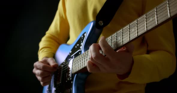 Male Guitarist in a Yellow Jumper Plays an Electric Guitar on Black Background
