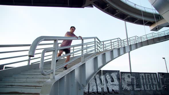 a Freerunner Jumping Off a High Ladder Onto Gravel Against the Background of Graffiti Under a Bridge alt