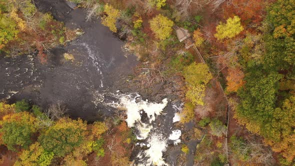 A top down shot directly above a waterfall, surrounded by colorful fall foliage in upstate NY. The c alt