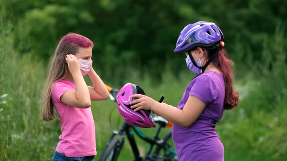 Two little girls in pink and purple helmets and medical masks. 