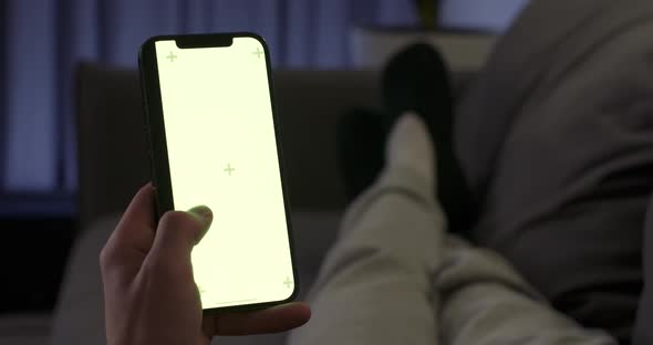 Young Man Lying on the Sofa in Living Room Man Rests on the Sofa and Uses Smartphone Scrolls Through alt