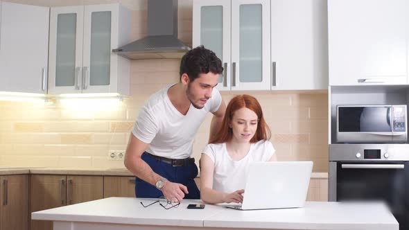 Business Couple Looking at Laptop at Home in Kitchen.