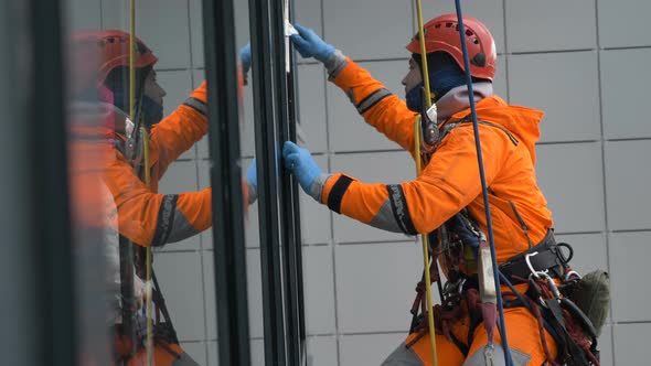 Professional Man Climber in Helmet Washes Windows at High Altitude Building, Slow Motion alt