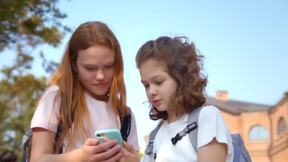 Portrait of Cheerful Preteen Girls Using Smartphone Standing Outdoors alt