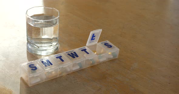 A prescription pill box organizer full of medicine, health vitamins and supplements with a glass of alt