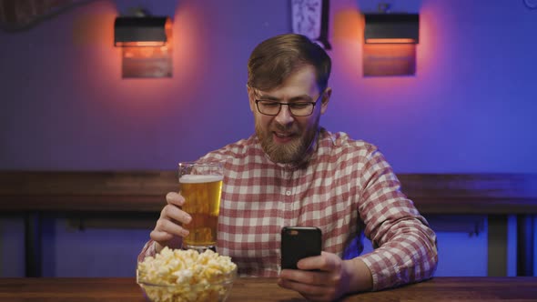 Portrait of Laughing Man with Beard and in Glasses Seeing Something Funny on Mobile Phone in Pub alt