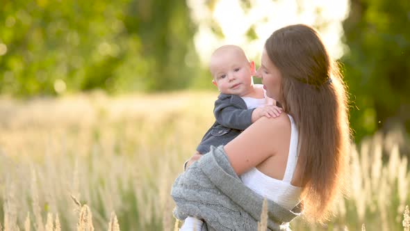 Loving tender mum in a dress with a cute little baby on a field at sunset
